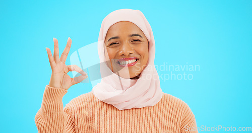 Image of Muslim woman, ok sign and smile on face with hand for emoji, icon or agreement. Islamic female with hijab and symbol for thank you, support and agreement or approval on a studio blue background