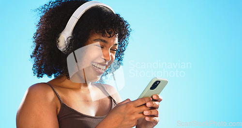 Image of Black woman, phone and headphones isolated on blue background listening to music, social media video or funny meme. Happy gen z person laughing for audio tech, internet post and cellphone in studio