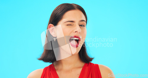 Image of Happy, woman and winking face on blue background, studio and color backdrop. Portrait, female model and smile for wink, secret and girl in fun mood, red cosmetics and personality for flirting emoji