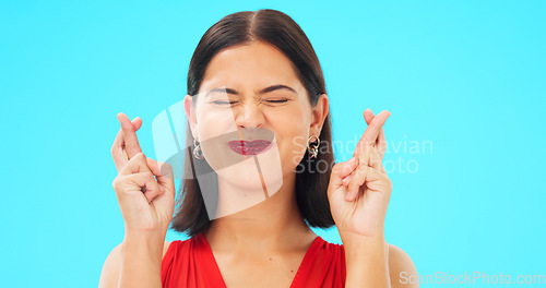 Image of Happy, woman and face with fingers crossed on blue background, studio and wishing for good luck. Portrait of excited female model hope for winning prize, optimism and smile for emoji, hands and sign