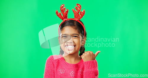 Image of Christmas, green screen and a girl in a reindeer antlers headband pointing towards chromakey space. Portrait, kids and holidays with an adorable little female child on blank space feeling festive