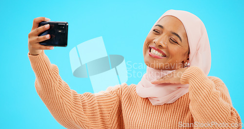 Image of Selfie of muslim woman isolated on blue background for social media kiss, smile and emoji post online. Face of happy islamic gen z or hijab person in profile picture or influencer lifestyle in studio