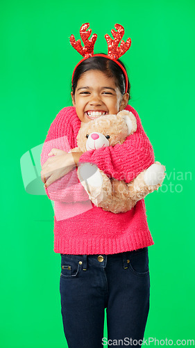 Image of Christmas, teddy bear and happy with girl in green screen studio for hugging, celebration and festive. Present, cheerful and vacation with child on background for season, holiday and happiness