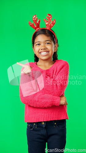 Image of Child, christmas and pointing at space on green screen with finger or hand. Smile portrait of excited girl kid on studio background with antlers headband for holiday celebration mockup with hands