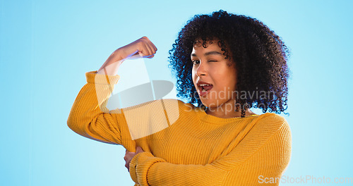 Image of Wink, arm and bicep with a black woman joking in studio on a blue background for fun or humor. Playful, strong and muscle with an attractive young female comic flexing while winking or laughing