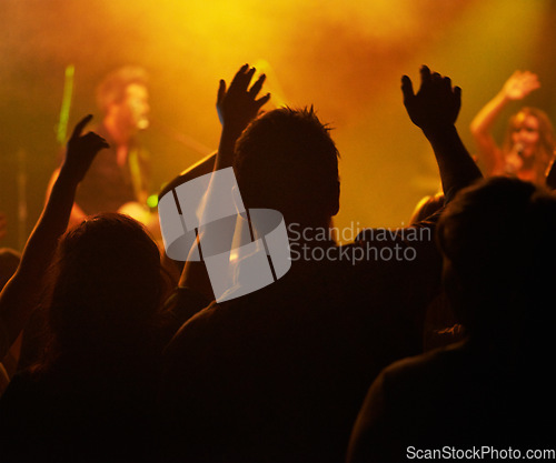 Image of Fans, hands and silhouette, people at concert or music festival from back, orange lights and energy at live event. Dance, fun and excited crowd in arena at rock band performance or audience dancing.