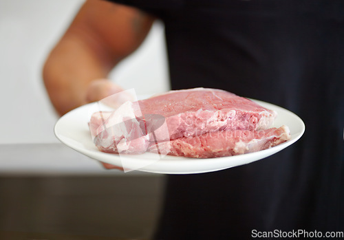 Image of Food, protein and a plate of raw steak in the hand of a man for diet, nutrition or meal preparation. Kitchen, cooking and meat with a strong male bodybuilder eating beef for a healthy lifestyle