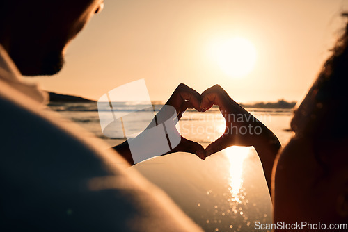 Image of Sunset, beach and couple with a heart symbol while on a vacation, adventure or weekend trip. Romance, silhouette and closeup of man and woman with love hand gesture in the evening on romantic holiday