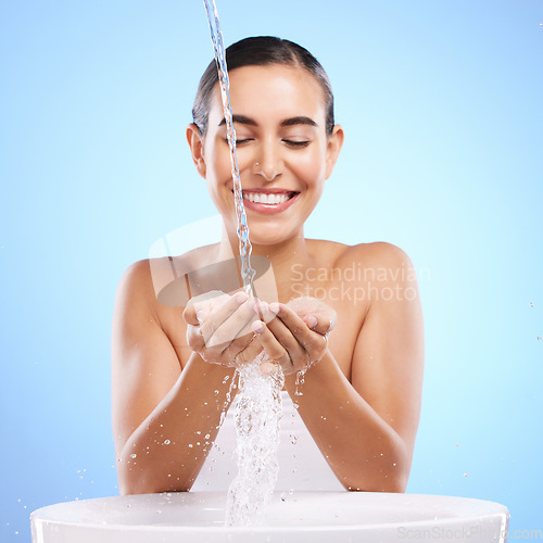 Image of Woman, hands and water splash with smile for skincare hygiene, wash or facial treatment in sink against blue studio background. Happy female smiling in natural beauty cleanse, minerals or self care