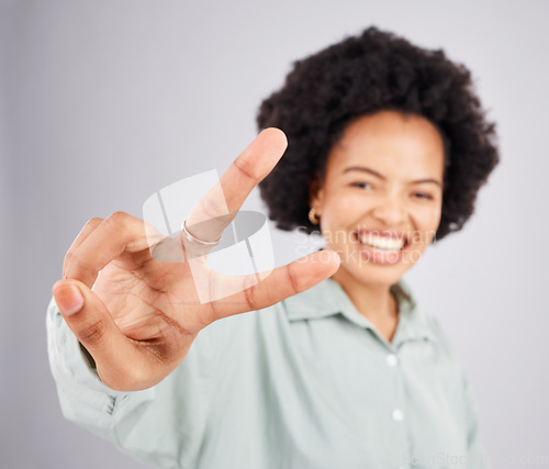 Image of Portrait, peace and hand gesture with a woman in studio on a gray background feeling happy or carefree. Smile, emoji and sign with a happy young female indoor for freedom, wellness or good vibes