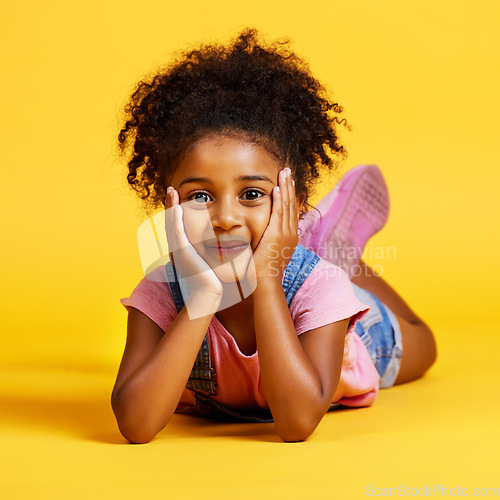 Image of Smile, cute and portrait of a child on the floor isolated on a yellow background in a studio. Adorable, sweet and an innocent girl lying down looking happy, beautiful and relaxed on a backdrop