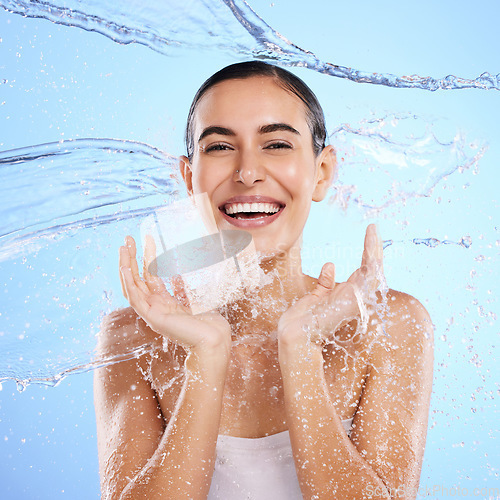 Image of Water splash, portrait and happy woman cleaning on blue background, studio and excited for wellness skincare. Female model, smile and shower for beauty, facial hydration and aqua on color backdrop