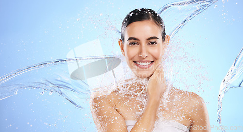 Image of Water splash, portrait and woman shower in studio, blue background and healthy beauty of wellness skincare. Happy female model, wet and cleaning for hygiene, hydration and smile on color backdrop