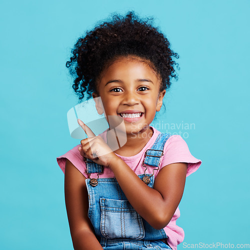Image of Portrait, pointing and mockup with a girl on a blue background in studio showing product placement space. Kids, marketing and advertising with an adorable female child indoor to point at branding