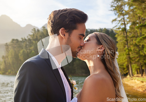 Image of Love, wedding and kiss with a newlywed couple by a lake outdoor in celebration of marriage or romance. Water, summer and a bride and groom kissing while bonding together in tradition after ceremony