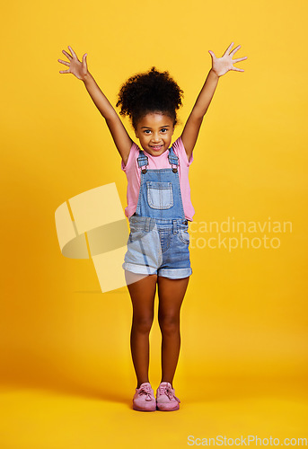 Image of Studio, portrait and excited child with hands up and a smile on face on yellow background. Happy young girl kid model with happiness, carefree and positive attitude for surprise sale announcement