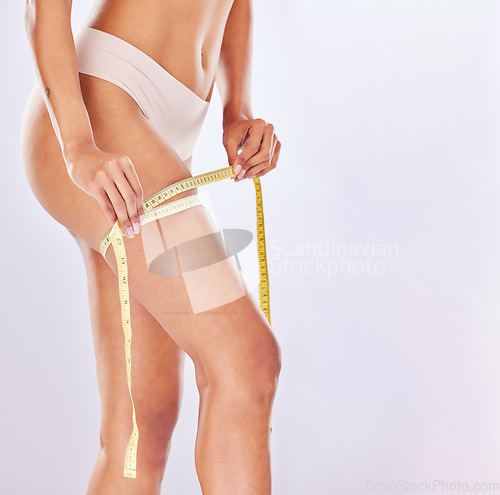 Image of Health, weight loss and woman with measuring tape on legs for diet, wellness and exercise on white background. Beauty, fitness and girl in underwear for liposuction, cosmetic surgery and slimming