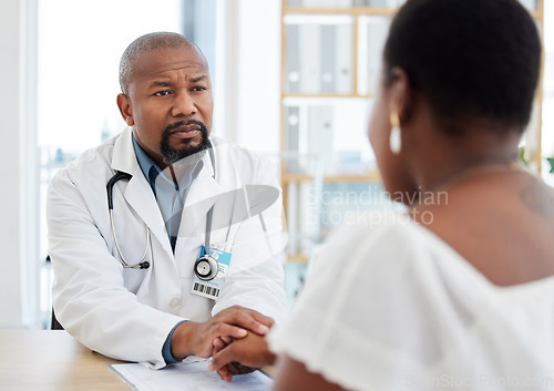 Image of Serious doctor, patient and holding hands in consultation for bad news, cancer diagnosis or comfort. Healthcare, black man and medical professional with woman for help, support and empathy in clinic.