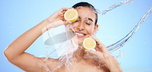 Image of Beauty, lemon and water splash with woman in studio for natural cosmetics, nutrition and detox. Glow, fruits and hydration with female on blue background for diet, clean face and vitamin c skincare