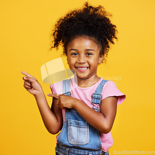 Image of Portrait, studio and happy child pointing hand at space with a smile on face on yellow background. Young girl kid with happiness, carefree and positive attitude to show product placement mockup deal
