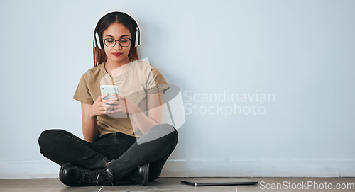 Image of Music headphones, floor and woman with phone in home by wall background with mockup. Cellphone, social media and female sitting on ground while streaming or listening to podcast, radio sound or audio