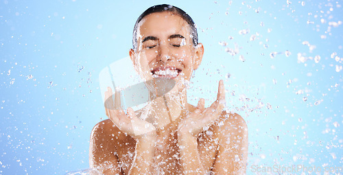 Image of Water splash, face and woman shower in studio, blue background and healthy beauty of wellness skincare. Happy female model, wet drops and cleaning of facial, aqua hydration or smile on color backdrop