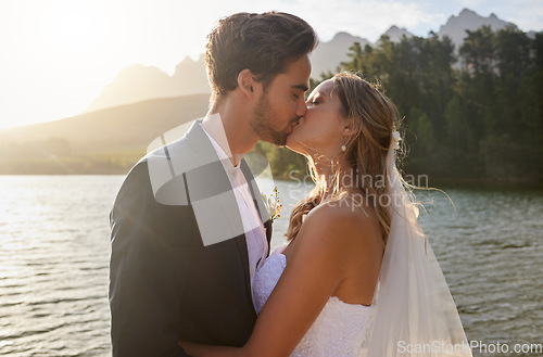 Image of Love, wedding and a newlywed couple kissing by a lake outdoor in celebration of their marriage for romance. Water, summer or kiss with a bride and groom bonding together in tradition after ceremony