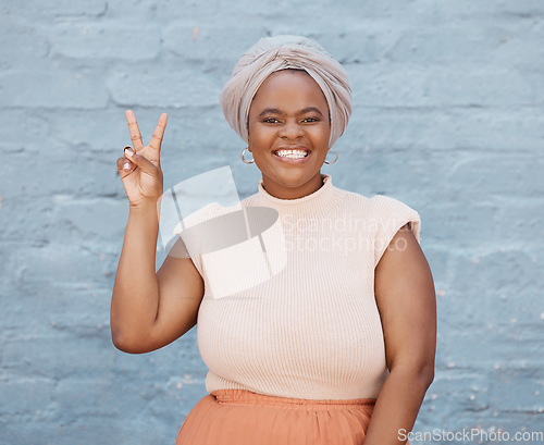 Image of Portrait, peace and hand gesture with a business black woman on a blue brick wall with a smile. Hand, emoji and motivation with a female employee showing a v sign while feeling positive or confident