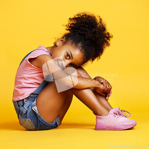 Image of Portrait, shy and girl child on studio floor for children fashion, playful and sweet against yellow background. Face, little and smile by kid with self love, pose and relax while sitting isolated