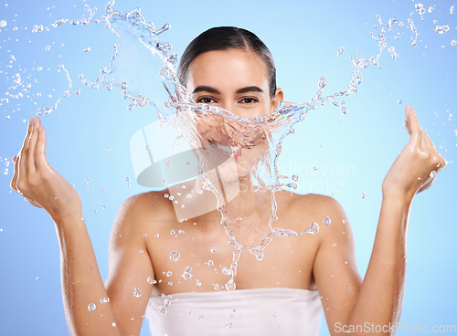 Image of Water splash, portrait or happy woman and face wash for skincare or hygiene on blue background in studio. Smile, wet or model and clean hands in wellness washing, beauty grooming or facial treatment