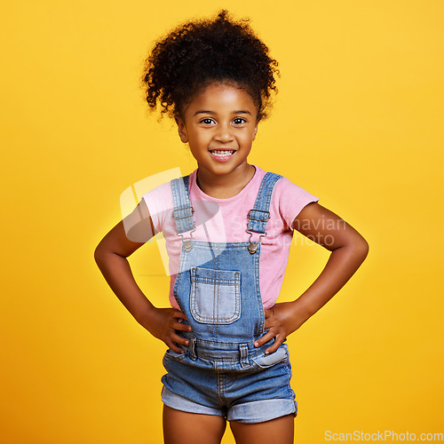 Image of Happy, portrait and child with a smile on face isolated on a yellow background. Cute young girl kid model with happiness, carefree and positive attitude in studio with hands on hips and mockup