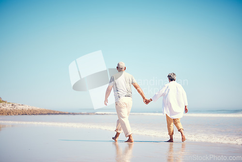 Image of Holding hands, beach and an old couple walking outdoor in summer with blue sky mockup from behind. Love, romance or mock up with a senior man and woman taking a walk on the sand by the ocean or sea