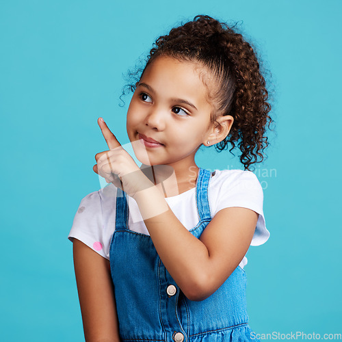 Image of Girl child, thinking and point in studio with idea, looking and young with mind development by blue background. Female kid, pointing finger and focus with fashion, kids clothes or mindset by backdrop