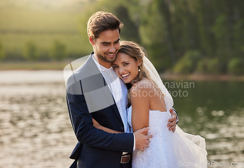 Image of Happy wedding couple, hug and smile by water lake for romantic honeymoon getaway in nature. Man and woman hugging in happiness for marriage relationship or embracing loving commitment in the outdoors