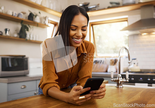 Image of Happy woman, phone text and kitchen in a home reading a web app. House, female and smile of a young person with joy resting on a counter top table feeling relax typing with mobile networking