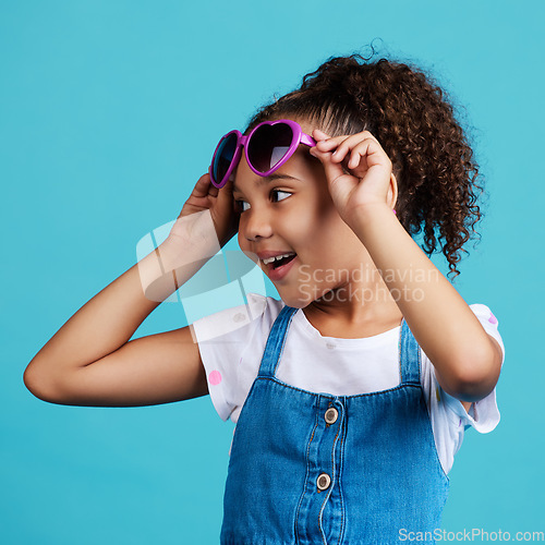 Image of Happy, smile and of a child with sunglasses in studio with positive, energy and excited face expression. Happiness, childhood and girl kid model with funky, trendy and cool glasses by blue background