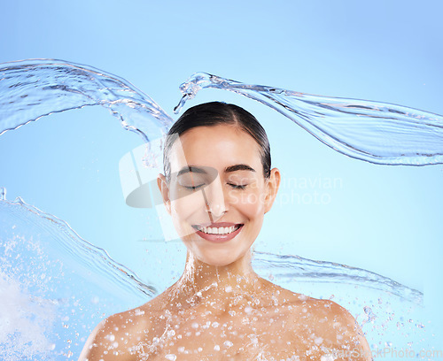 Image of Water splash, smile and woman cleaning in studio, blue background and healthy beauty of wellness skincare. Happy female model, wet and shower for hygiene, facial hydration and face on color backdrop