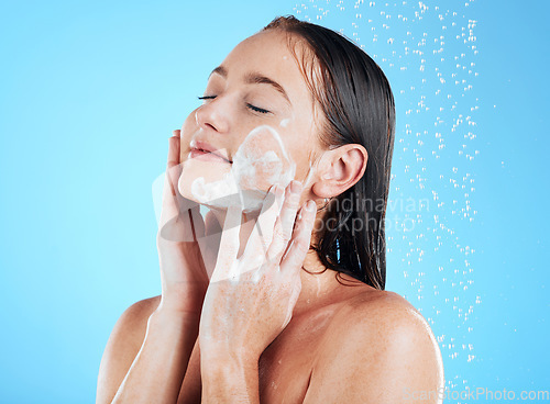 Image of Shower, facial and woman washing face with soap on blue background for grooming, cleaning and wellness. Skincare, bathroom and happy girl with foam product for hygiene, hydration and beauty in studio