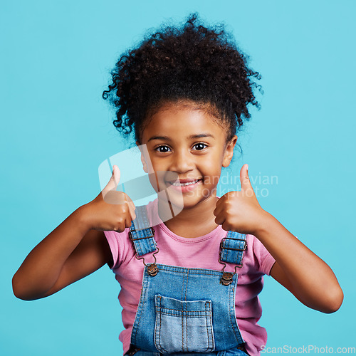 Image of Little girl, portrait smile and thumbs up for winning, good job or success against a blue studio background. Happy child face smiling showing hand thumb emoji, yes sign or like for agreement or win