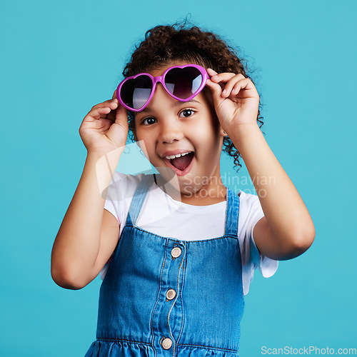 Image of Happy, sunglasses and portrait of a child in studio with a positive, shocked and excited face expression. Happiness, surprise and girl kid model with funky, trendy and cool glasses by blue background