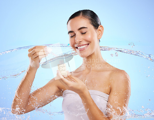 Image of Happy woman, dropper and water splash for skincare serum, product or cream against a blue studio background. Calm female smile holding pipette for beauty cosmetics, essential oil or facial treatment