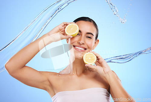 Image of Vitamin c, lemon and water splash with portrait of woman in studio for natural cosmetics, nutrition and detox. Glow, fruits and hydration with female on blue background for diet, face and skincare