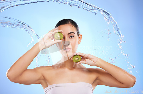 Image of Kiwi, portrait and water splash of woman, beauty and wellness on studio blue background. Female model, shower and healthy fruits for natural benefits, detox skincare and dermatology of diet nutrition