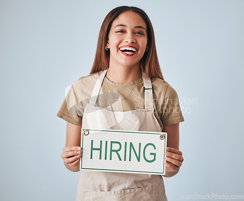 Image of Happy woman, portrait and hiring sign for small business recruitment, career or job opportunity against a gray studio background. Female entrepreneur with apron holding billboard or poster for hire