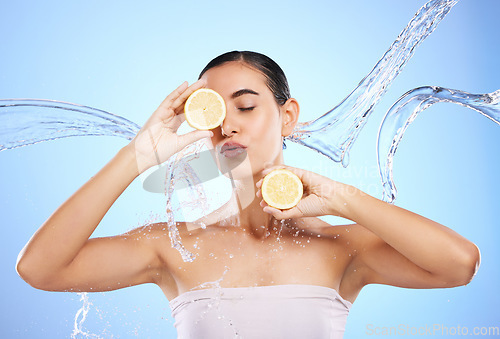 Image of Beauty, skincare and water splash with woman and lemon in studio for natural cosmetics, nutrition or mockup. Wet, fruits and hydration for female on blue background for diet, face or citrus vitamin c