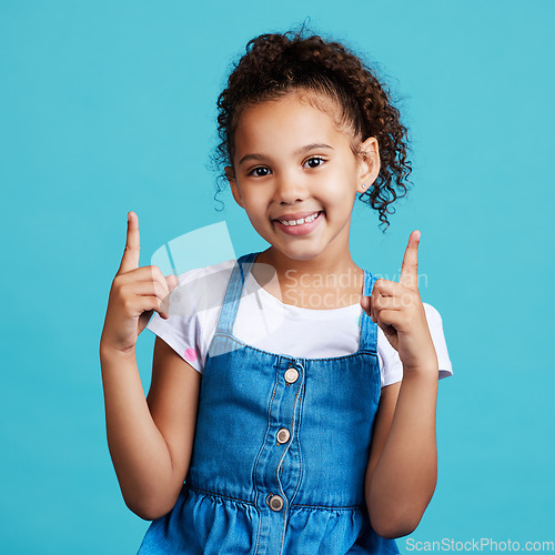 Image of Portrait, point and mockup with a girl on a blue background in studio showing product placement space. Kids, marketing and advertising with an adorable female child pointing at branding indoor