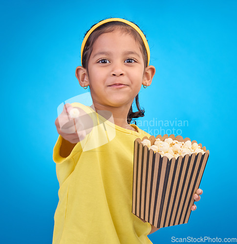Image of Popcorn, offer and smile with portrait of girl and giving snack to you for food, cinema and relax. Friendly, movie and film with child eating for streaming, subscription and tv on blue background