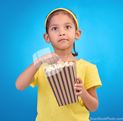 Image of Popcorn, eating and watching movie with girl in studio for food, cinema and relax. Television, focus and film with child and snack for streaming, subscription and tv isolated on blue background