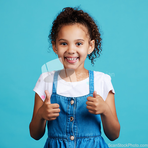 Image of Happy, thumbs up and portrait of a child in a studio with success, happiness and achievement. Smile, positive and face of a girl kid with a satisfaction or approval hand gesture by a blue background.