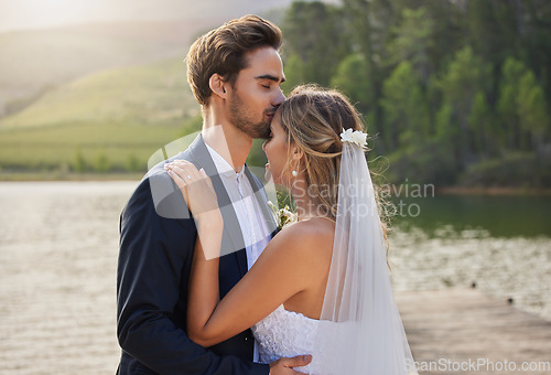 Image of Couple, wedding and forehead kiss by lake on romantic honeymoon or getaway together in nature. Man kissing woman on head and hugging for marriage, relationship or loving embrace in the outdoors